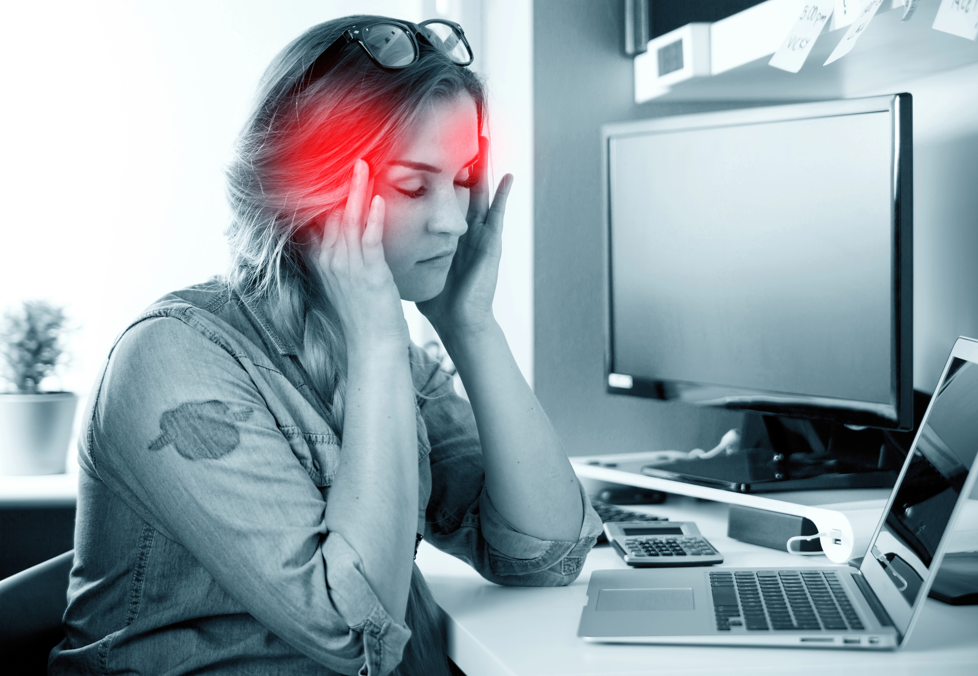 Woman massaging temples during migraine at her work desk